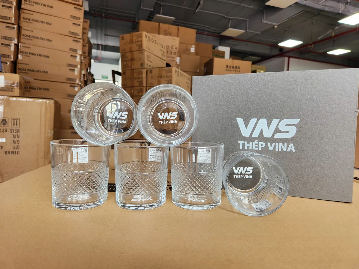 Sáu cốc thủy tinh thân trụ có họa tiết phần dưới và logo ở đáy, cạnh hộp xám