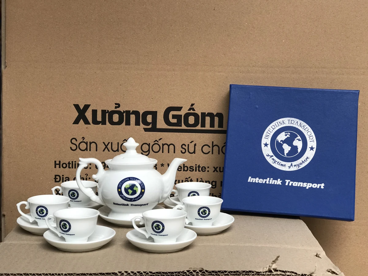 Bộ ấm chén trắng quai lượn có nhận diện hình tròn trên ấm, chén và hộp trong ảnh nguồn