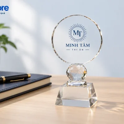 Mô phỏng biểu trưng mặt tròn MINH TÂM đặt trên bàn cạnh sổ và bút
