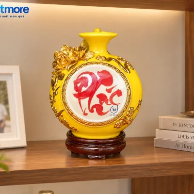 Mô phỏng bình chữ Phúc demo AN MINH đặt trên kệ gỗ trong tủ kính, cạnh khung ảnh và sách