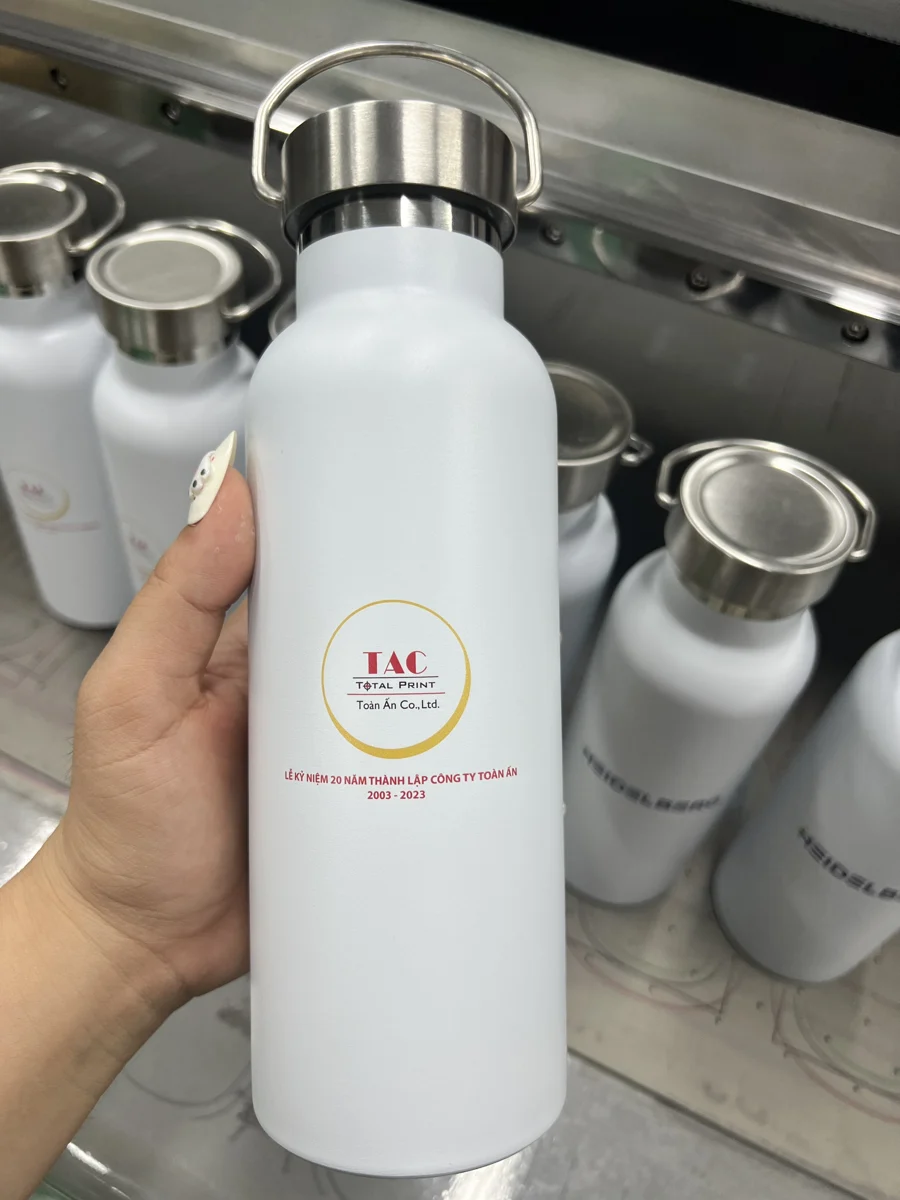 Bình trắng có nắp kim loại và quai cong đang được cầm trên tay