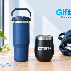 Bình xanh có quai và ly đen CAEX cạnh ba lô và sổ trên bàn