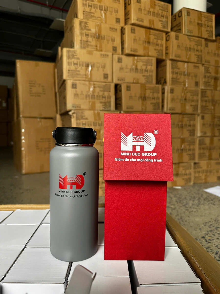 Bình màu xám và hộp đỏ in MINH DUC GROUP trước các kiện carton