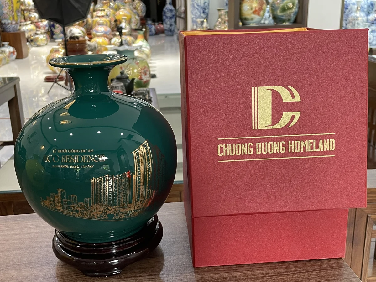 Bình xanh lá in hình công trình trên đế nâu cạnh hộp đỏ