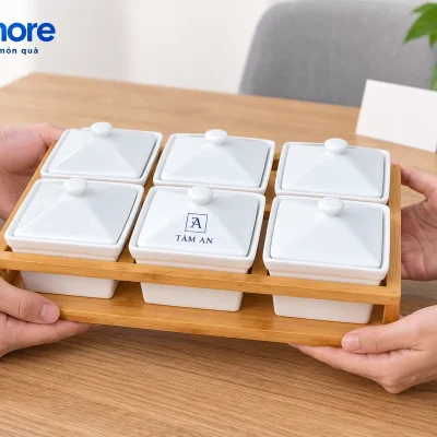 Hai người đỡ hai đầu và đáy khay khi trao bộ sáu hũ mứt trắng đóng nắp