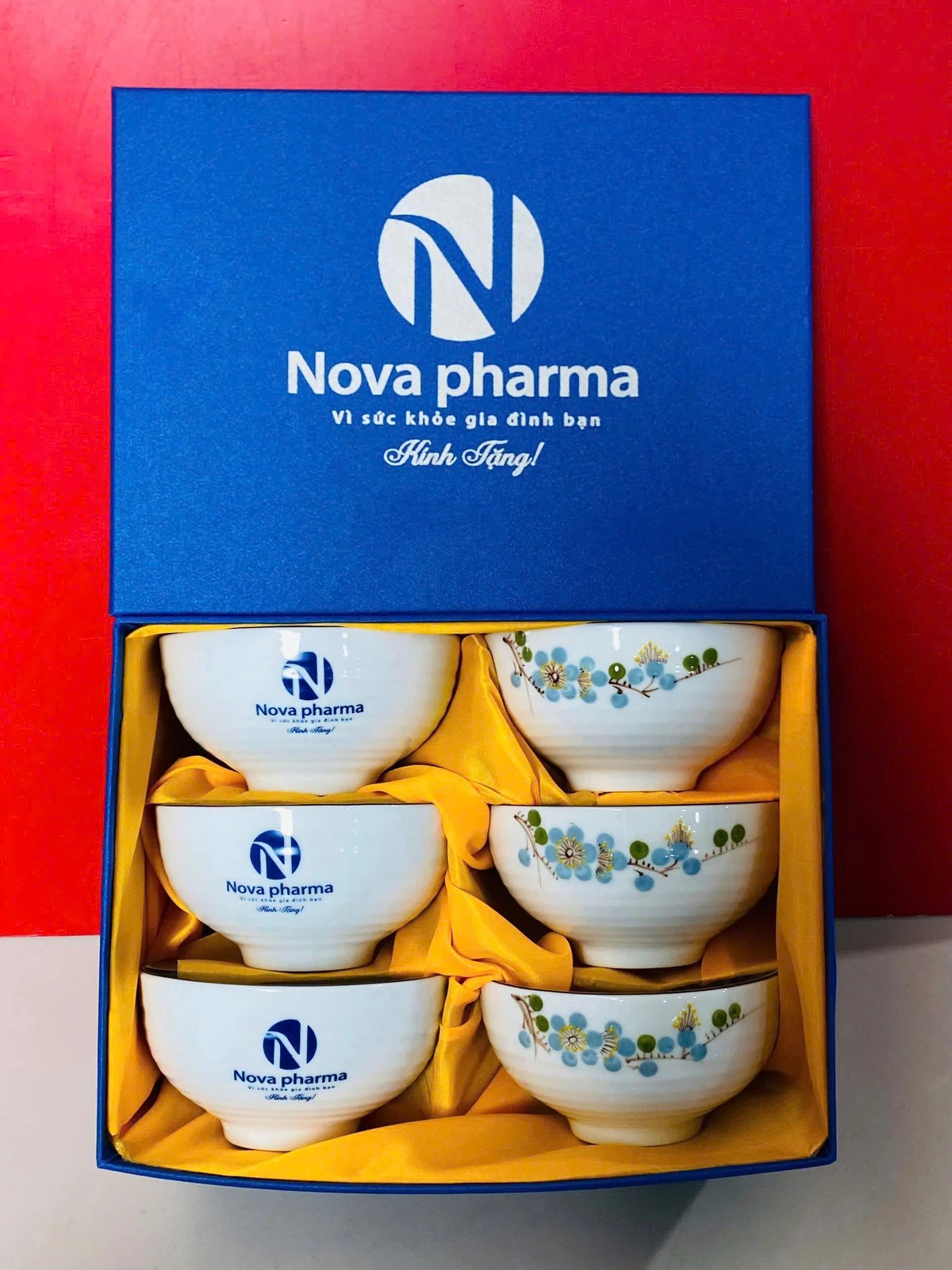 Hộp xanh lót vàng đựng sáu bát có nhận diện Nova pharma và hoa xanh