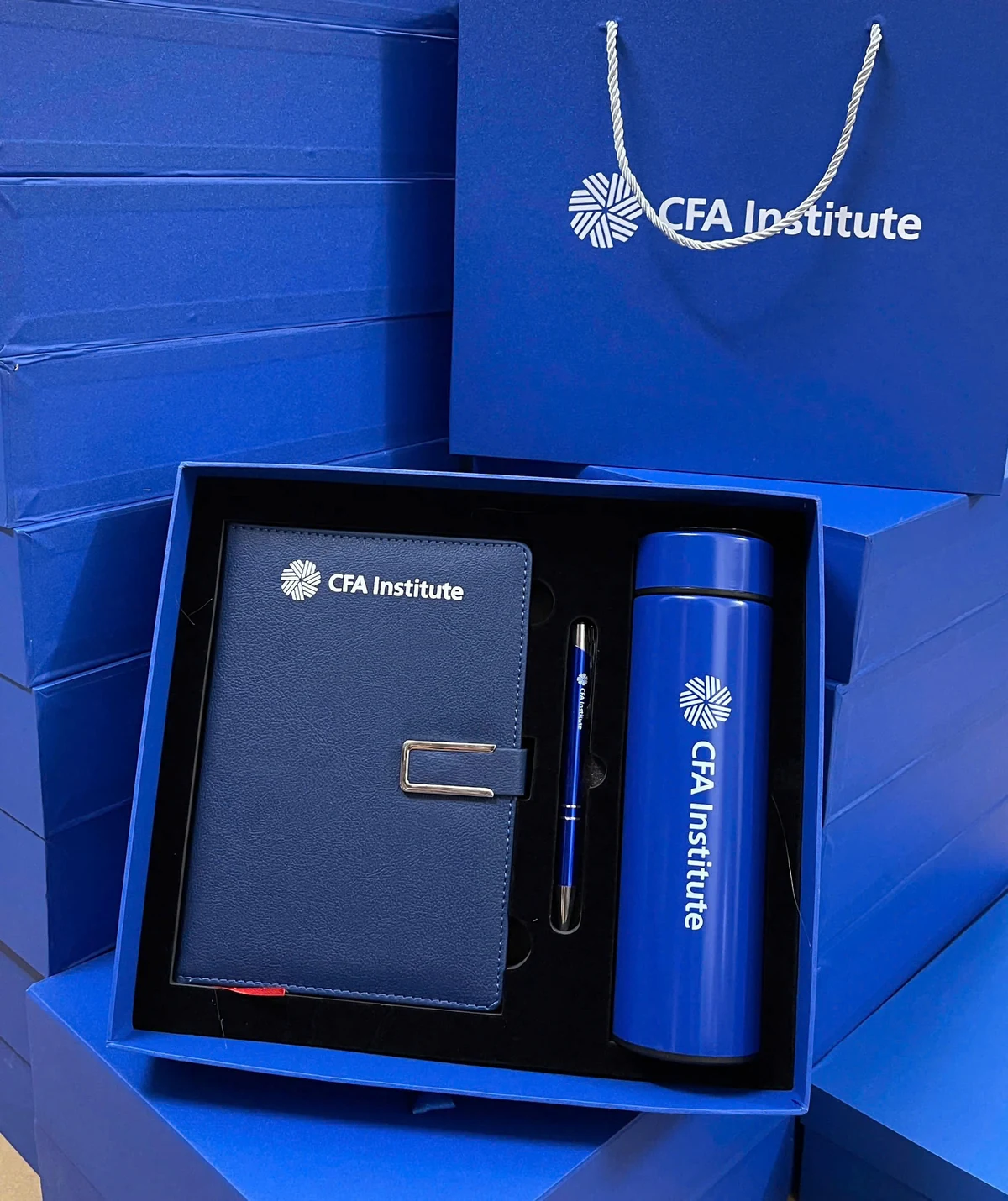 Ảnh gốc hộp xanh với sổ navy cài kim loại, bút và bình xanh in CFA Institute