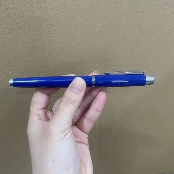 Ảnh gốc bút dạ bi xanh viền bạc đóng nắp được cầm ngang trên tay