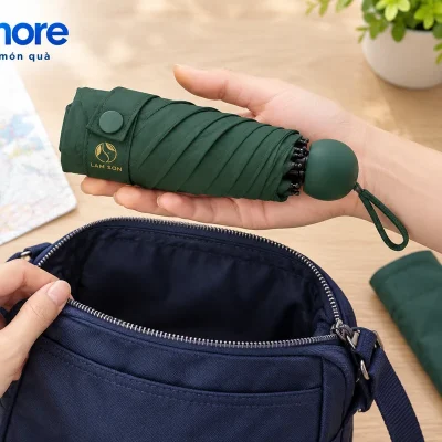 Mô phỏng dù xanh đậm đã gấp trên bàn tay phía trên túi đeo mở, cạnh bao vải xanh