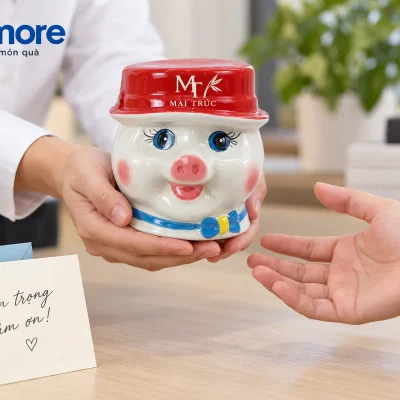 Mô phỏng người lớn trao heo đất mũ đỏ nhận diện MAI TRÚC cạnh thiệp cảm ơn