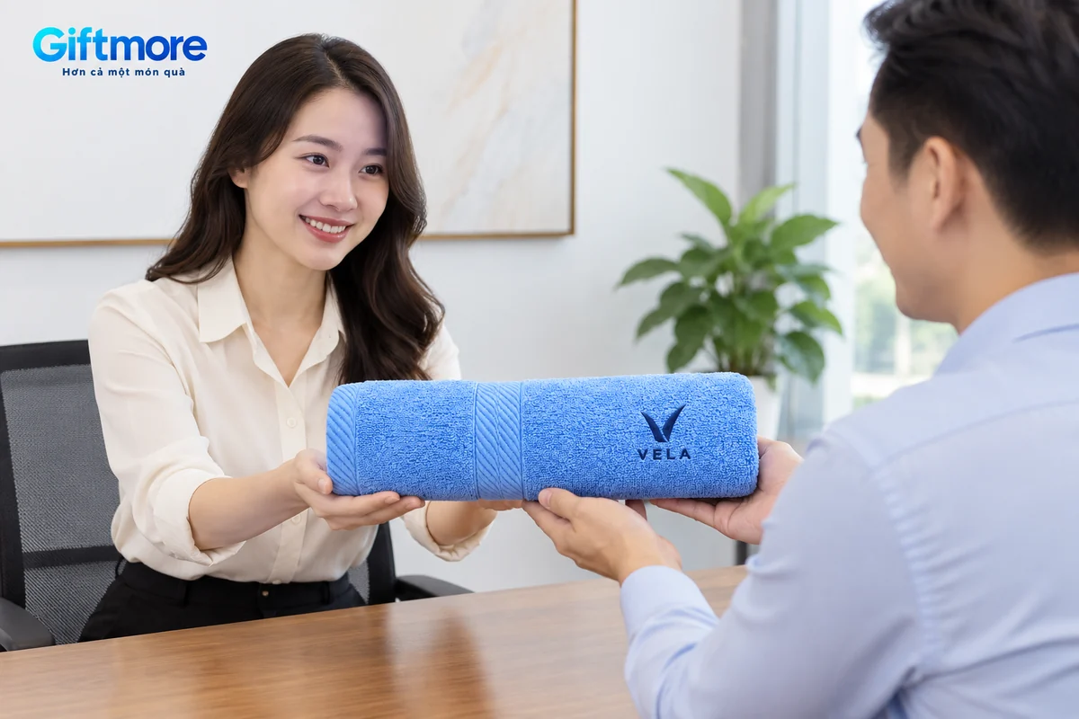 Mô phỏng trao một khăn cotton xanh gấp ngang thêu VELA tại văn phòng