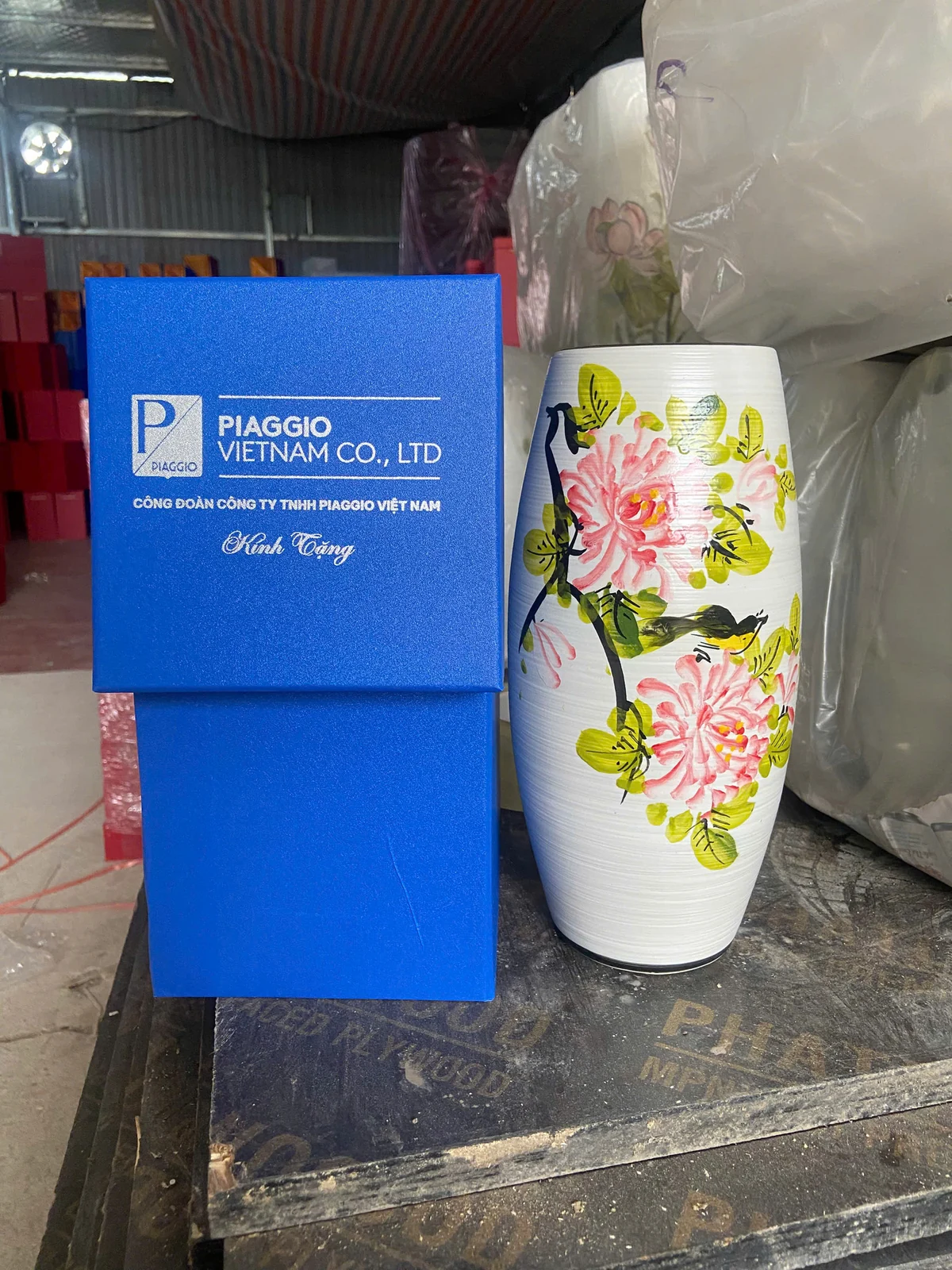 Lọ trắng họa tiết hoa hồng cạnh hộp xanh in PIAGGIO VIETNAM