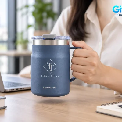 Mô phỏng người cầm quai ly Metro Mug navy tại bàn làm việc cạnh laptop